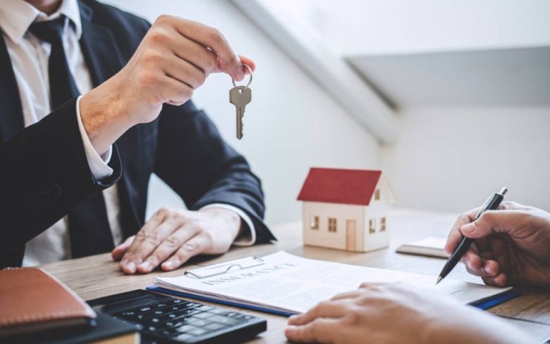 Real estate agent holding a key while a client signs a form